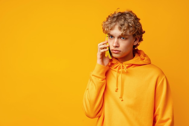 Jovem encaracolado falando no celular contra um fundo amarelo no estúdio