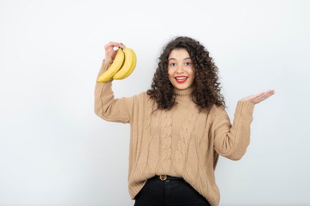 Foto jovem encaracolado segurando bananas sobre o branco.