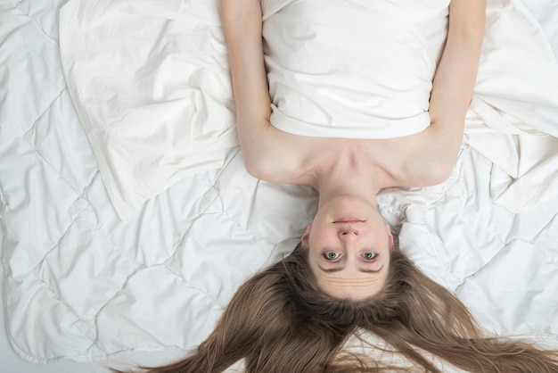 Jovem encontra-se na cama com os olhos abertos. Insônia. Distúrbios do sono. A menina não consegue dormir. Copie o espaço, vista superior.