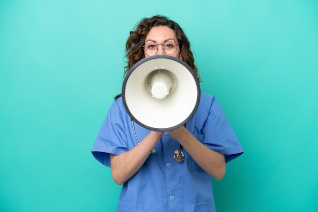 Jovem enfermeira caucasiana isolada em fundo azul gritando através de um megafone