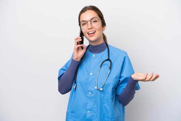 Jovem enfermeira caucasiana isolada em fundo branco, mantendo uma conversa com o celular com alguém