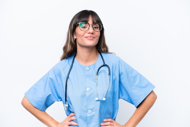 Jovem enfermeira caucasiana isolada em fundo branco posando com os braços no quadril e sorrindo