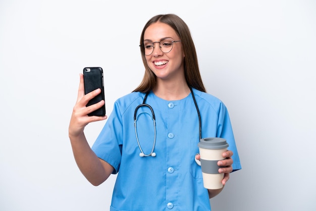 Jovem enfermeira caucasiana isolada em fundo branco segurando café para levar e um celular