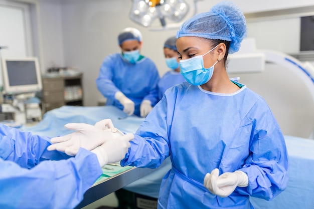 Jovem enfermeira com máscara protetora e vestuário de trabalho ajudando o cirurgião com luvas enquanto ambos se preparam para a operação