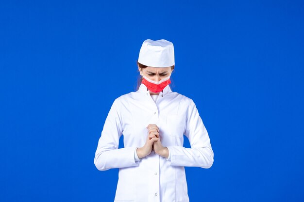 Jovem enfermeira de frente para um terno médico com máscara protetora vermelha na parede azul