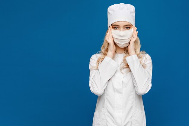 Jovem enfermeira em branco uniforme médico e máscara protetora posando