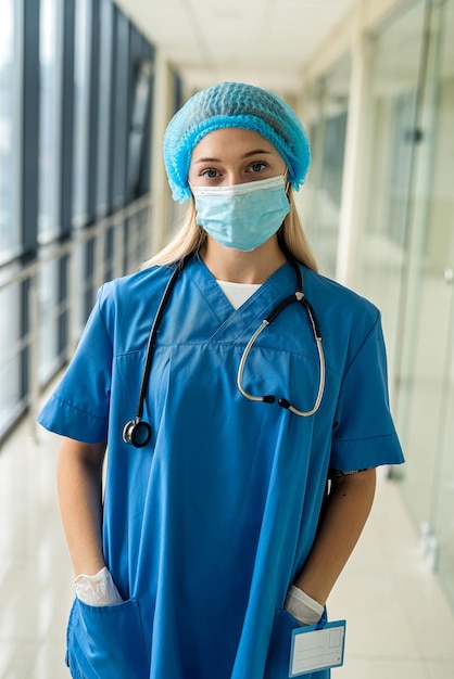 Jovem enfermeira em máscara uniforme com luvas com estetoscópio fica no hospital