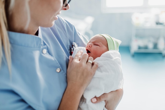 Jovem enfermeira em pé na maternidade e segurando o bebê recém-nascido nos braços. Após o conceito de nascimento.