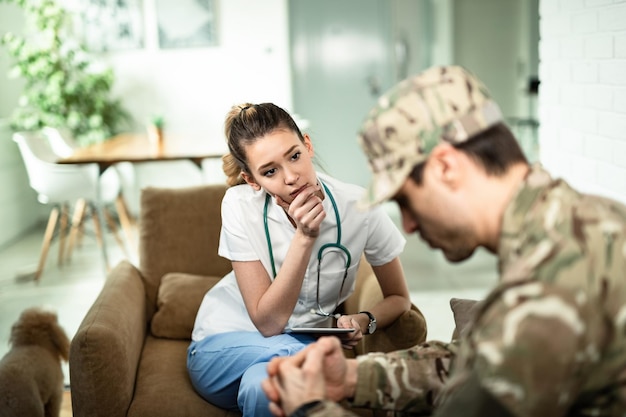 Jovem enfermeira preocupada se comunicando com o militar enquanto o visitava em casa