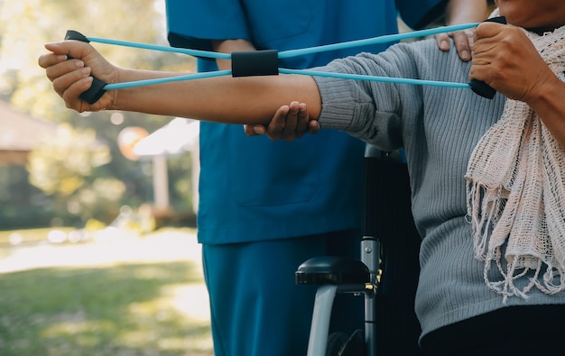 Jovem enfermeiro ou fisioterapeuta em roupão ajudando uma velhota aposentada feliz a fazer exercícios de fitness com halteres leves em casa Conceito de fisioterapia para idosos