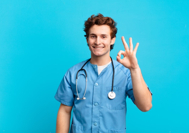 Jovem enfermeiro sentindo-se feliz, relaxado e satisfeito, mostrando aprovação com um gesto de ok, sorrindo