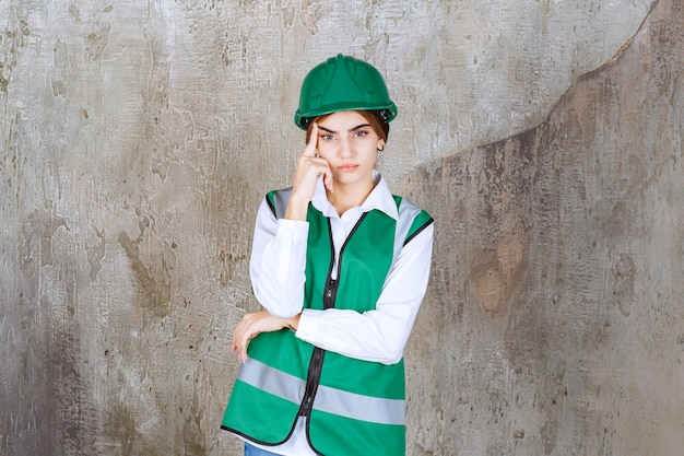 Jovem engenheira com colete verde e capacete em pé e posando