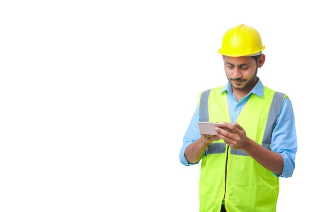 Jovem engenheiro indiano usando capacete e usando smartphone em fundo branco.