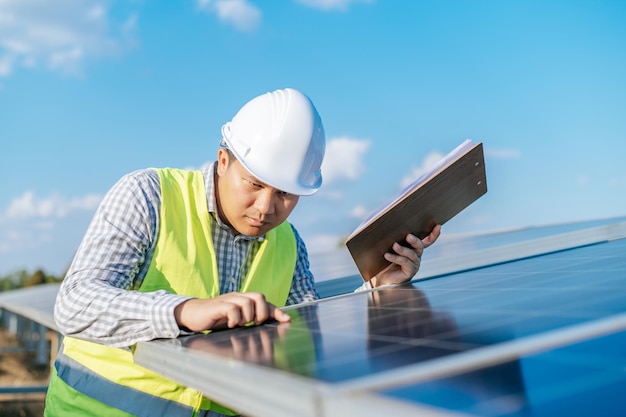 Jovem engenheiro inspetor asiático trabalhando na fazenda solar Técnico ou supervisor masculino no capacete branco Verificando a operação do sol e do painel solar fotovoltaico no espaço de cópia da estação