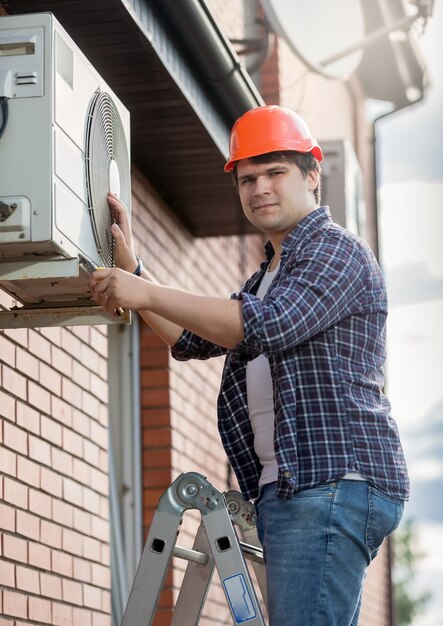 Jovem engenheiro instalando ar condicionado na parede externa do prédio