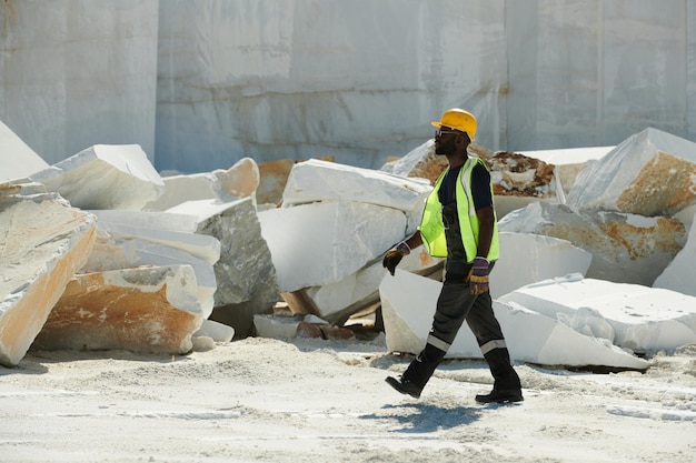 Jovem engenheiro masculino afro-americano em roupas de trabalho e capacete de segurança correndo para o local de trabalho