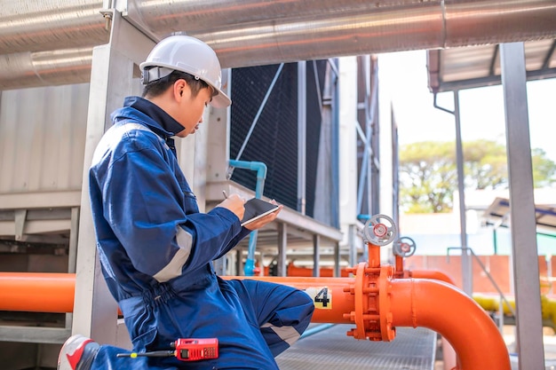 Jovem engenheiro trabalhando em grande fábricaTécnico em uniforme de proteção e com capacete de segurança, verificando a temperatura nos tubos