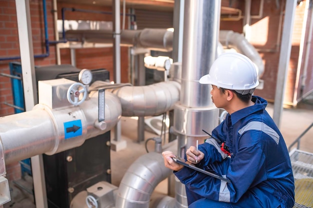 Jovem engenheiro trabalhando em grande fábricaTécnico em uniforme de proteção e com capacete de segurança, verificando a temperatura nos tubos