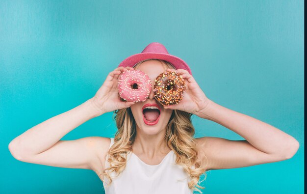 Jovem engraçada cobrindo os olhos com dois donuts