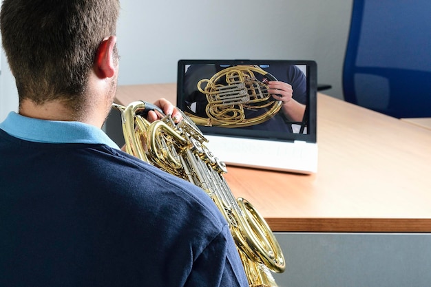 Jovem ensaia uma aula de música com um trombone em um laptop