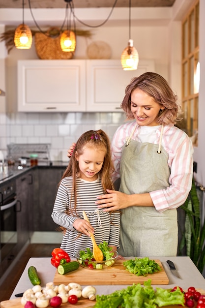 Jovem ensina a filha a misturar salada de vegetais frescos em uma cozinha moderna e iluminada