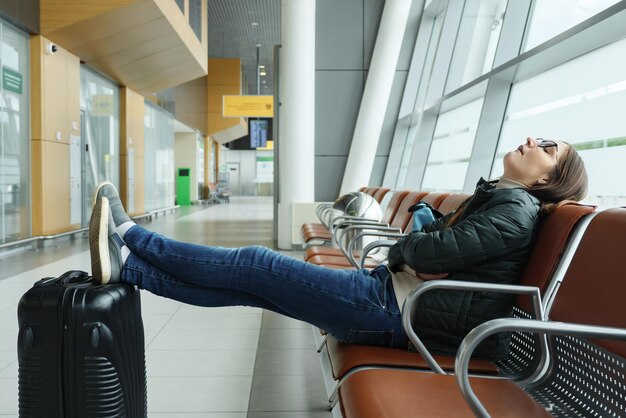 Foto jovem entediada e cansada está esperando seu voo no aeroporto sentado no corredor