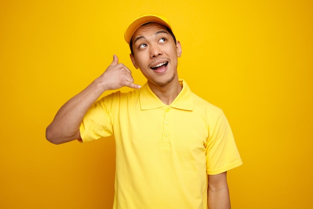 Jovem entregador animado usando boné e uniforme, olhando para cima, fazendo gesto de chamada