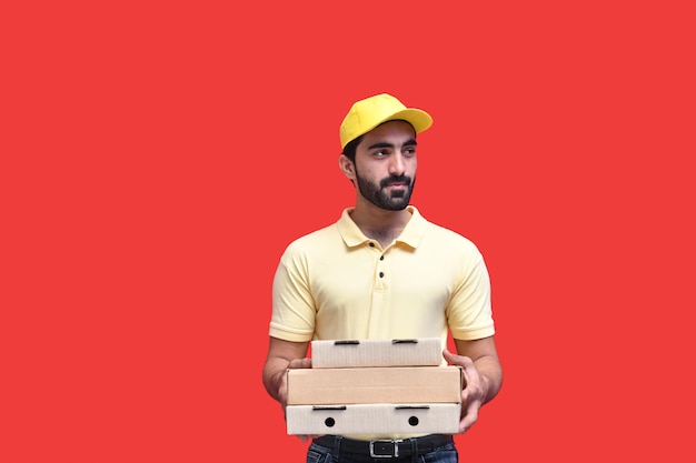 Jovem entregador de t-shirt amarela e boné segurando caixas de pizza modelo indiano do paquistanês