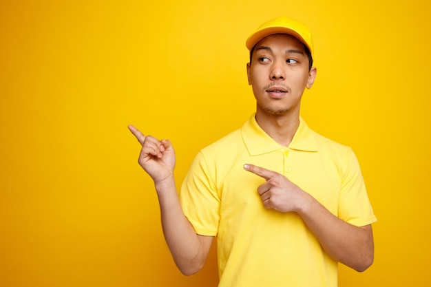 Jovem entregador impressionado de boné e uniforme, olhando para o lado apontando para cima no canto