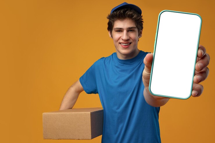 Foto jovem entregador mostrando smartphone com tela em branco no estúdio