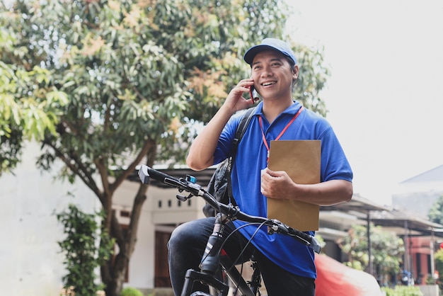Jovem entregador segurando envelope marrom com uma chamada na bicicleta