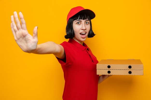 Jovem entregadora caucasiana animada segurando caixas de pizza e estendendo a mão