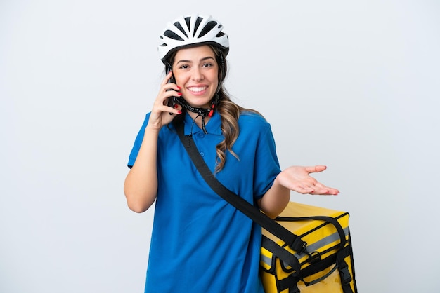 Jovem entregadora com mochila térmica isolada em fundo branco, mantendo uma conversa com o celular com alguém