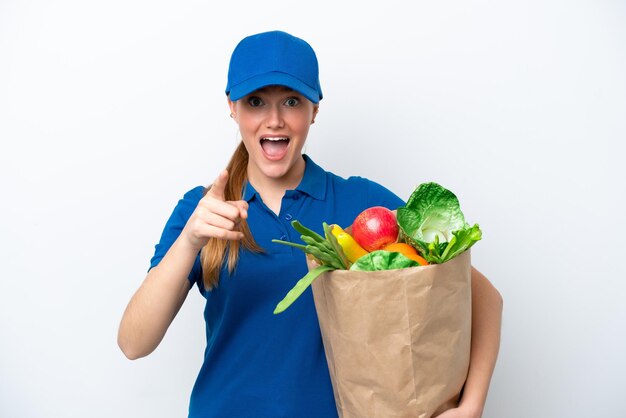 Foto jovem entregadora levando um saco de comida para viagem isolada no fundo branco surpreso e apontando para a frente