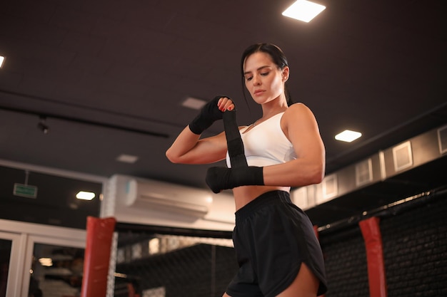 Jovem envolve seus punhos em bandagens pretas para luvas de kickboxing contra um salão de boxe preto