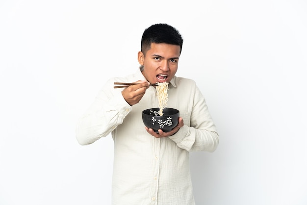 Jovem equatoriano isolado no fundo branco segurando uma tigela de macarrão com pauzinhos e comendo