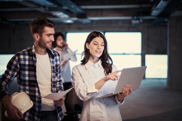 Jovem equipe de empresários em grupo, arquiteto e engenheiro no canteiro de obras, verificando documentos e fluxo de trabalho de negócios usando computador portátil no novo escritório de inicialização