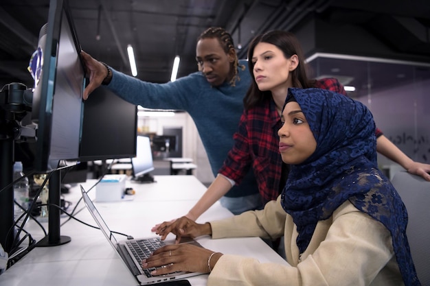 jovem equipe multiétnica de desenvolvedores de software trabalhando juntos usando um laptop enquanto escrevem código de programação em um escritório moderno