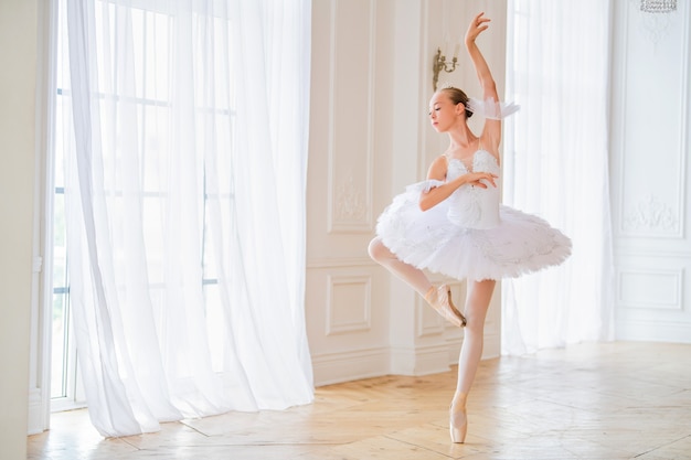 Jovem esbelta bailarina em um tutu branco em sapatilhas de ponta está dançando em um grande salão branco bonito.