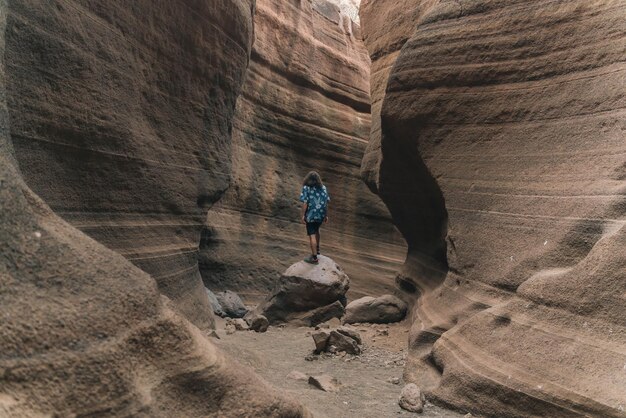 Foto jovem escalando uma rocha no meio de um desfiladeiro deserto olhando para cima