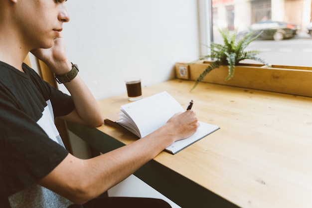 Jovem, escrevendo informações para o bloco de notas e falando do telefone móvel, adolescente planeja uma programação