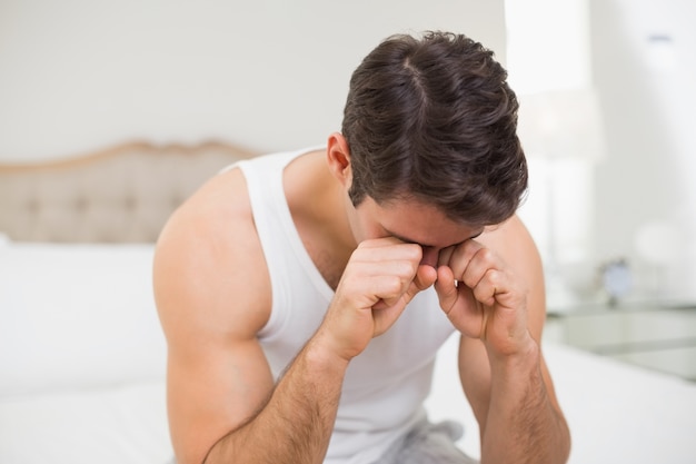 Jovem esfregando os olhos na cama