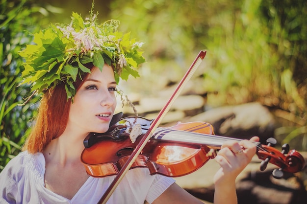 Jovem eslava tocando violino na floresta