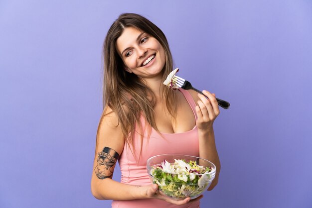 Foto jovem eslovaca isolada em roxo segurando uma tigela de salada e olhando para ela com expressão feliz