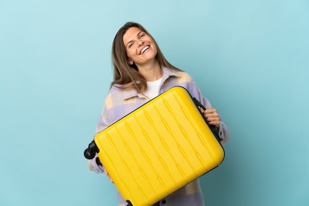 Jovem eslovaca isolada em um fundo azul de férias com uma mala de viagem