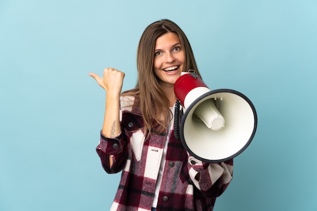 Jovem eslovaca isolada na parede azul gritando em um megafone e apontando para o lado