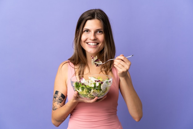 Jovem eslovaca isolada no roxo segurando uma tigela de salada com uma expressão feliz