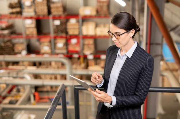 Jovem especialista em uma grande planta industrial rolando em um tablet enquanto navega na rede em busca de dados técnicos no local de trabalho