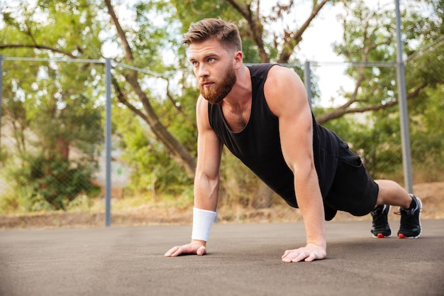 Jovem esportista barbudo atraente fazendo flexões ao ar livre