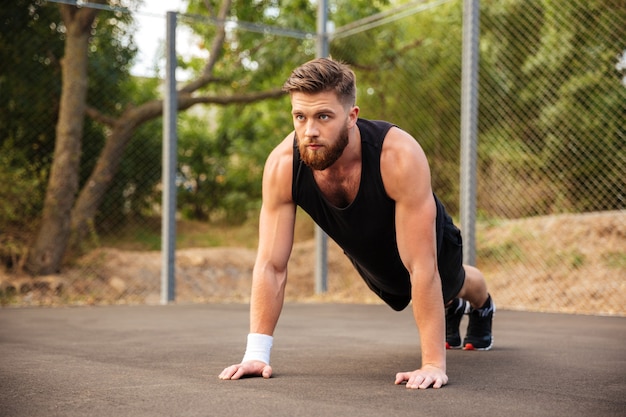 Jovem esportista barbudo bonito fazendo flexões ao ar livre